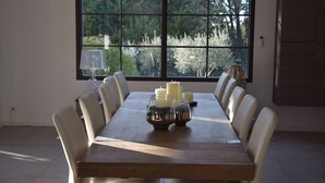 Une table à manger, agrémentée de bougies et de verres, entourée de chaises, dans une pièce dotée d’une grande fenêtre et d’un buffet.