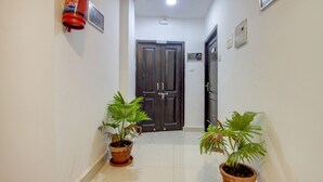 A hallway with two potted plants, a fire extinguisher, and a door with a sign above it. - Treebo Trip Lazy Holidays (Arpora)