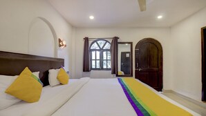 A bedroom with a large bed, a window with curtains, a door, and a ceiling fan. - Treebo Trip Lazy Holidays (Arpora)