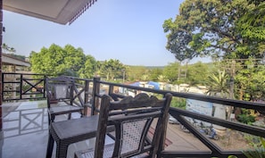 A balcony with wicker furniture, a clear view of the surrounding greenery and buildings, and a tiled floor. - Treebo Trip Lazy Holidays (Arpora)