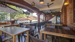 An outdoor dining area with wooden tables and chairs, ceiling fans, and hanging lights. - Treebo Trip Lazy Holidays (Arpora)