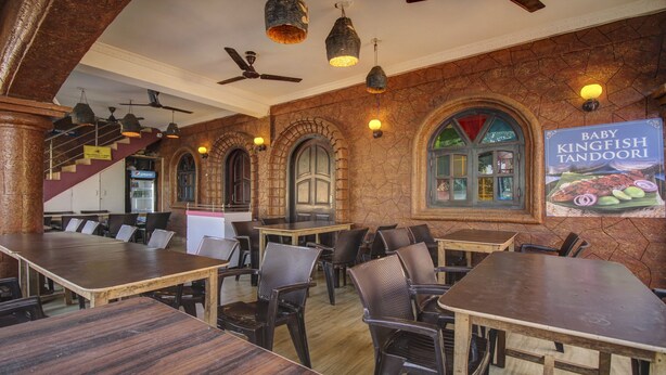 A restaurant with high ceilings, exposed brick walls, and arched windows. Tables and chairs are arranged for dining. - Treebo Trip Lazy Holidays (Arpora)