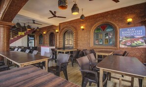 A restaurant with high ceilings, exposed brick walls, and arched windows. Tables and chairs are arranged for dining. - Treebo Trip Lazy Holidays (Arpora)