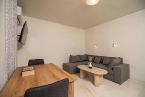 Una sala moderna con una mesa de comedor de madera, un sofá gris, una mesa de centro redonda y un televisor de pantalla plana montado en la pared.