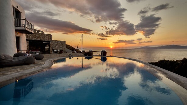 A swimming pool with a sunset view, stone architecture, and outdoor seating. - Asimina (Mykonos)