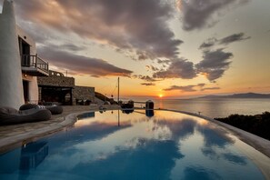 Una piscina con vistas a la puesta de sol, arquitectura de piedra y mobiliario exterior.