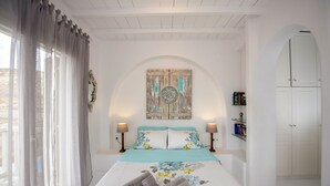 A bedroom with a bed, curtains, a wall clock, a bookshelf, and a wardrobe. - Asimina (Mykonos)