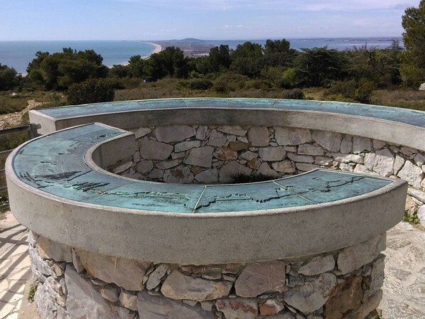 Une structure circulaire en pierre, surmontée d’un toit métallique et entourée d’un mur de pierre, qui offre une vue panoramique sur le paysage côtier.
