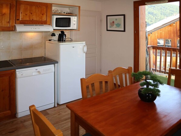 A compact kitchen with a microwave, dishwasher, and wooden cabinets. There is a dining table with chairs and a potted plant. - Charming 2BR Apt for 6 with Pool, Jacuzzi & Balcony - Les Orres (Les Orres)