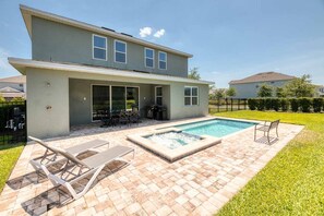 A two-story house with a backyard patio, a swimming pool, and outdoor furniture.
