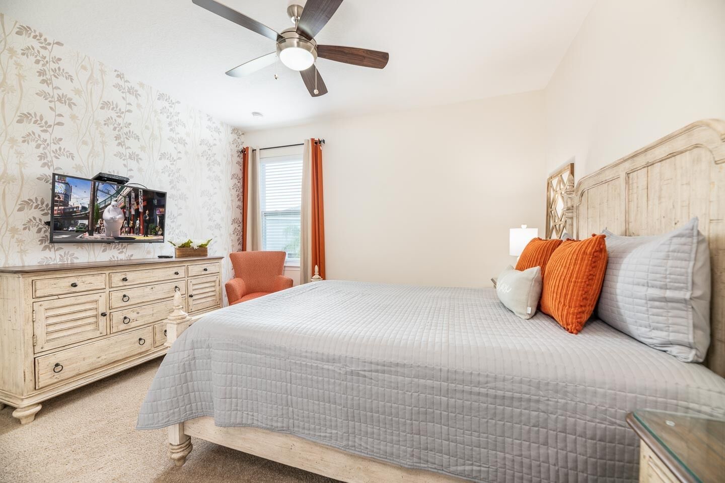 Quarto com cama, cômoda, televisão e ventoinha no teto.
