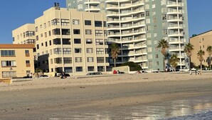 Ein Strandhotel mit mehreren Etagen, Balkonen und einem Sandstrand im Vordergrund.