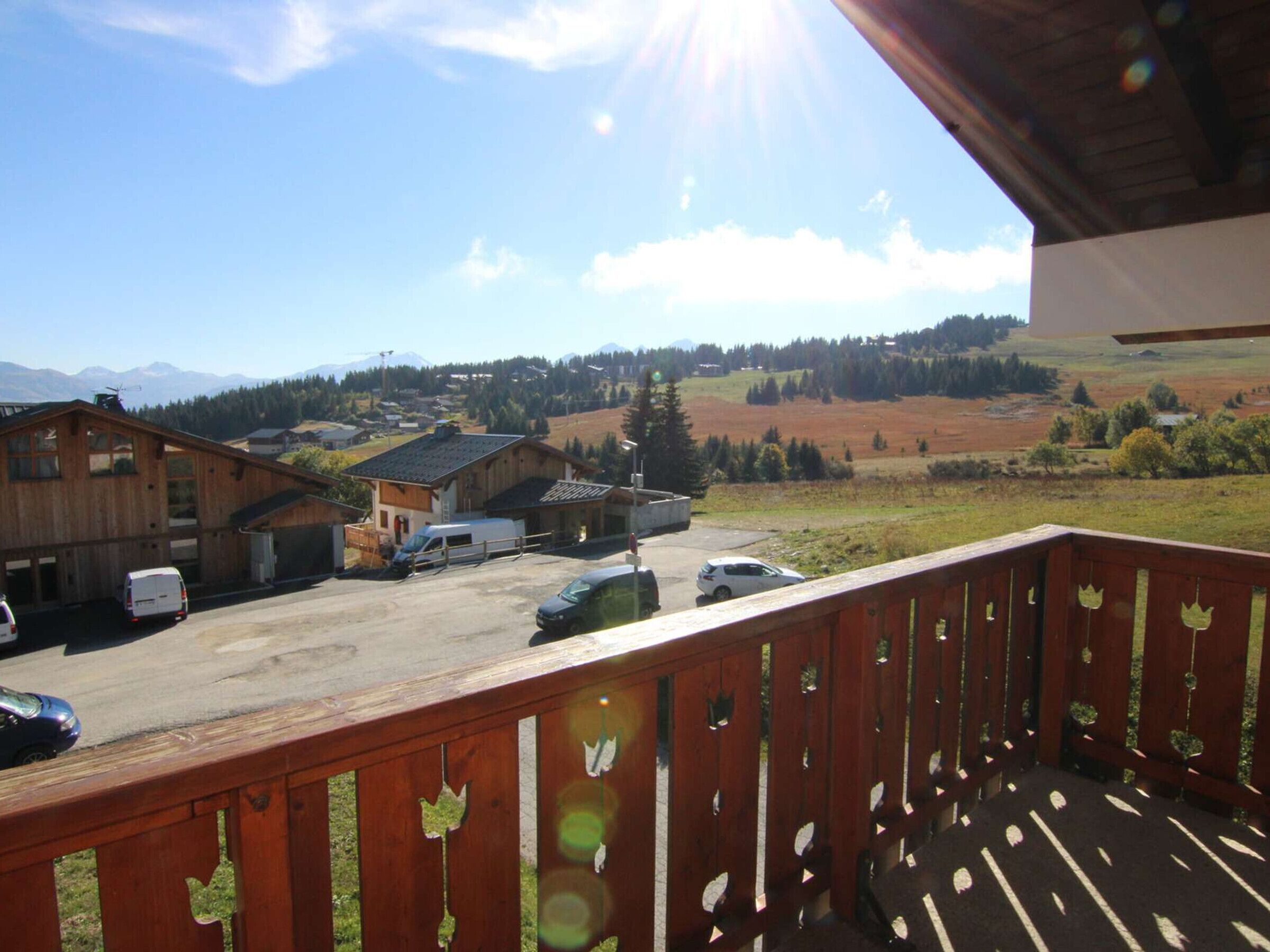 A wooden building with a balcony overlooking a parking area and a scenic landscape with mountains in the distance.