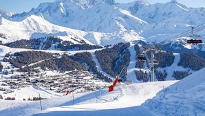 A snow-covered mountain landscape with a ski lift, a ski resort with buildings, and a clear sky.