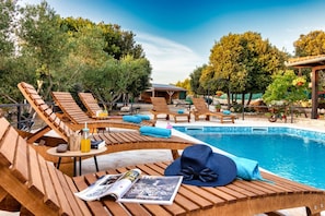 Un espace aménagé au bord de la piscine, avec des chaises longues en bois, une piscine et un petit bâtiment en arrière-plan.
