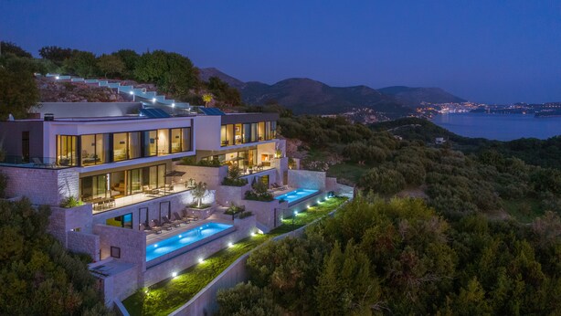 Una casa moderna de varios pisos, con piscina, amplias ventanas y vistas al mar y las colinas.