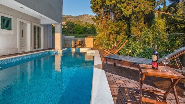 Una piscina con bordo in legno e lettini, immersa nel verde con montagne sullo sfondo.