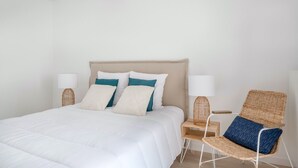 A neatly arranged bedroom with a large bed, two bedside tables, and a wicker chair. - Flat for 4 by the sea in Pléneuf-Val-André (Pléneuf-Val-André)