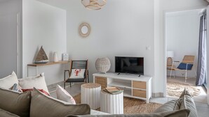 A modern living room with a white sofa, a television on a white cabinet, a wicker chair, and a round side table. - Flat for 4 by the sea in Pléneuf-Val-André (Pléneuf-Val-André)