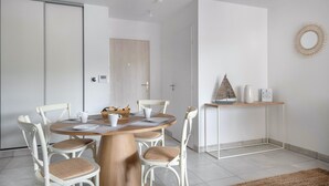 A modern dining area with a round wooden table, white chairs, and a small side table with decorative items. - Flat for 4 by the sea in Pléneuf-Val-André (Pléneuf-Val-André)