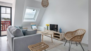 A modern loft apartment with a large window, a sofa, a TV, and wicker furniture. - Flat for 6 50m from the beach (Pléneuf-Val-André)