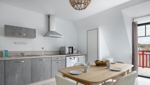 A modern kitchen with grey cabinets, a wooden dining table, and a view of the beach through the window. - Flat for 6 50m from the beach (Pléneuf-Val-André)