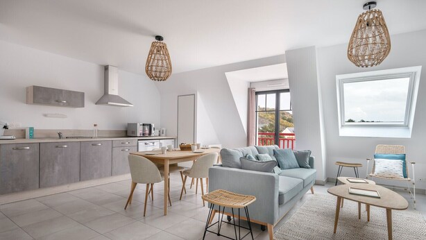 A modern kitchen with grey cabinets, a dining table with chairs, a grey sofa, and a wicker chair. There are two hanging wicker lamps and a large window with a view. - Flat for 6 50m from the beach (Pléneuf-Val-André)