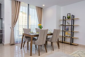 A dining area with a table set for four, surrounded by chairs, and a bookshelf with decorative items. - MekongView 6 CondoTel (Phnom Penh)