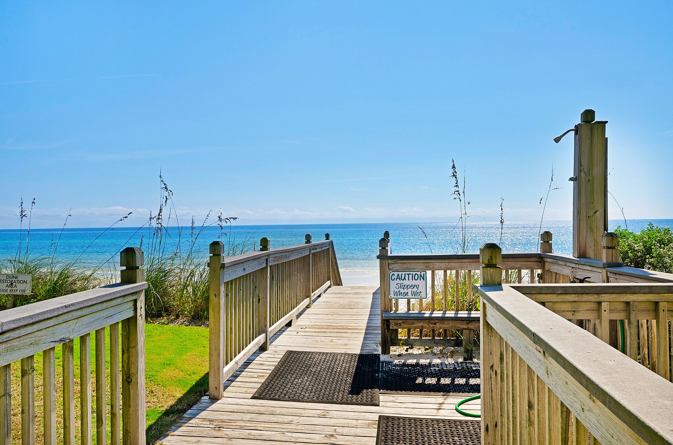 A wooden boardwalk leading to a beach with a caution sign for slippery conditions when wet.