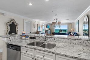 A kitchen with a granite countertop, stainless steel sink, and white cabinetry.