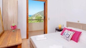 Un dormitorio con cama, mesita de noche, mesa de madera y vista a un balcón con paisaje montañoso.