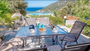 Un área de comedor al aire libre con mesa y sillas, con vista a una piscina y al mar.
