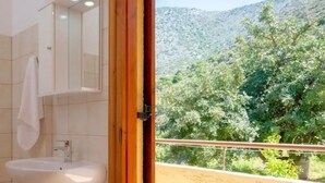 Un baño con lavamanos y espejo, y vista a un paisaje montañoso a través de una puerta abierta.