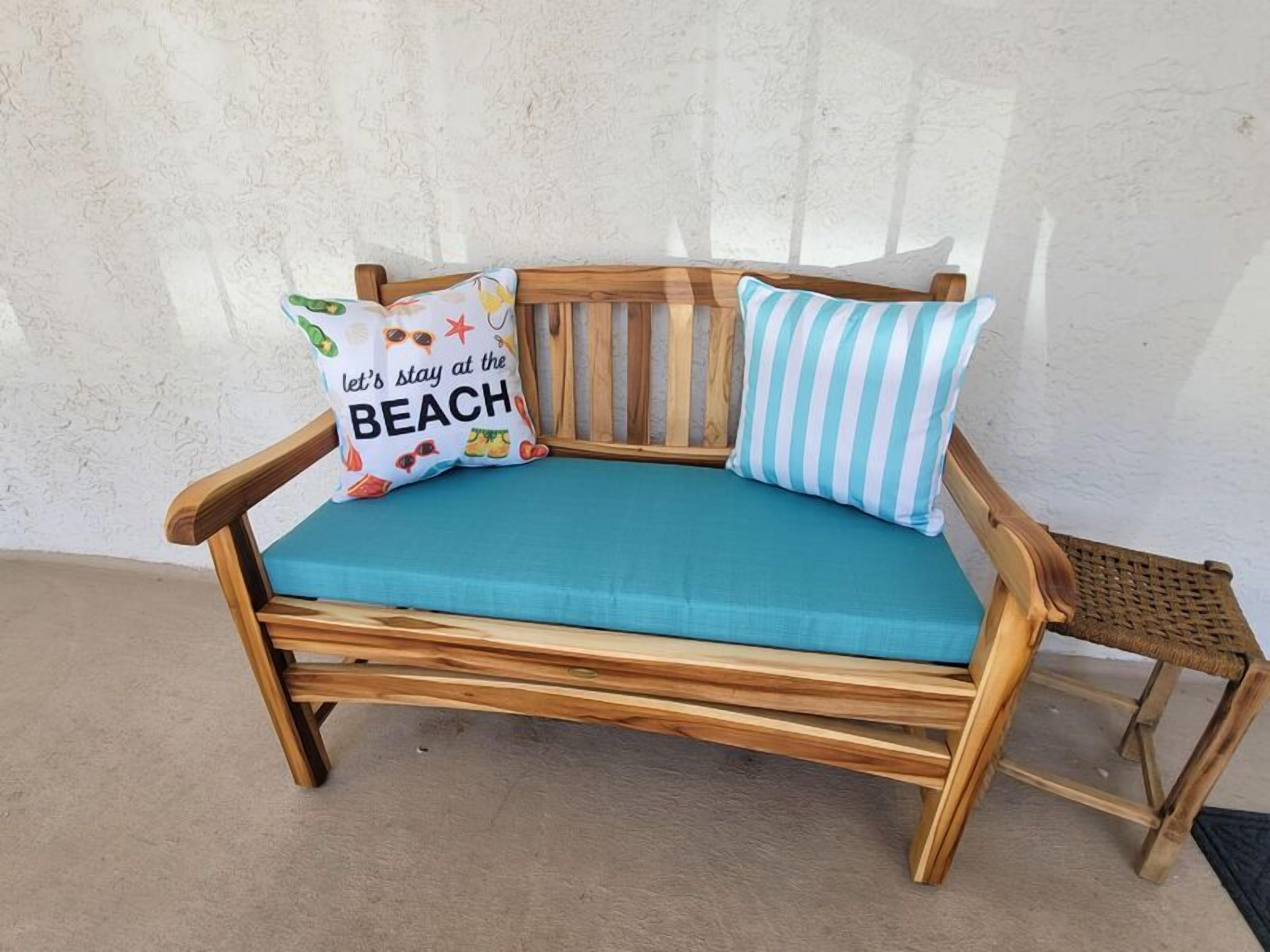 Een houten bank met een zeegroene kussen en twee sierkussens, waarvan er één een ontwerp heeft met een strandthema.
