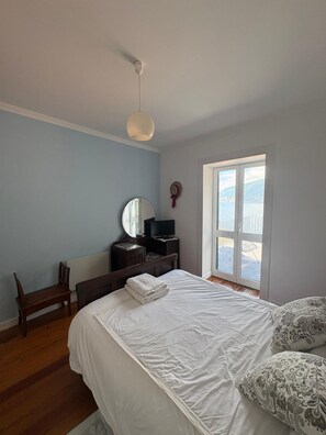 Ein Schlafzimmer mit Bett, Kommode, Spiegel, Stuhl und Fenster mit Aussicht.