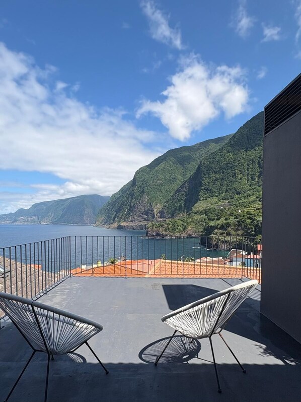 A balcony with two chairs, a view of the sea, and a mountainous landscape.