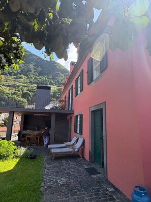 A red building with a patio area, outdoor seating, and a view of a hilly landscape.