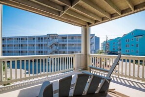 Un balcon offrant une vue sur un immeuble à plusieurs étages, une piscine et un ciel dégagé.