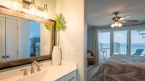 A hotel room with a large mirror, a white sink, a ceiling fan, and a bed with a view of the ocean.