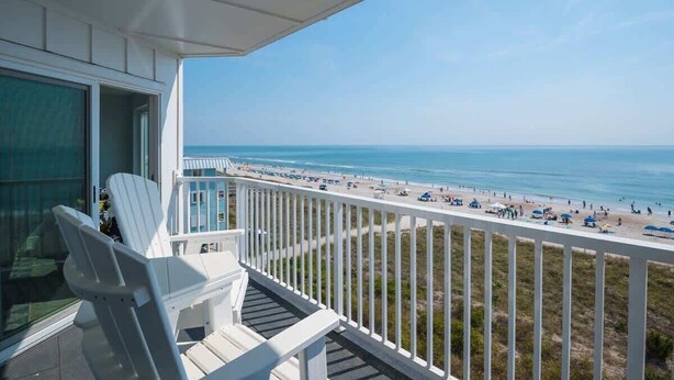 A balcony with white railings overlooking a beach.