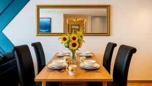 A dining area with a wooden table, black chairs, white plates, bowls, and a vase of sunflowers. A large mirror hangs on the wall above the table. - 2 bed 2 bath apartment in City Centre (Liverpool)