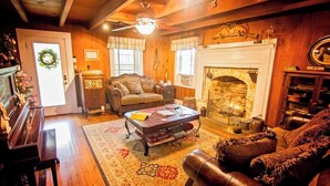 A cozy living room with a fireplace, wooden walls, a sofa, a coffee table, and a piano. - Fulkerson-Hilton historic homestead (Hiltons)