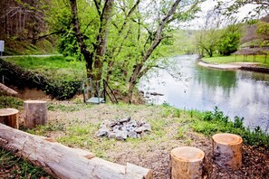 A riverside campsite with a fire pit, wooden stumps, and a metal railing. - Fulkerson-Hilton historic homestead (Hiltons)