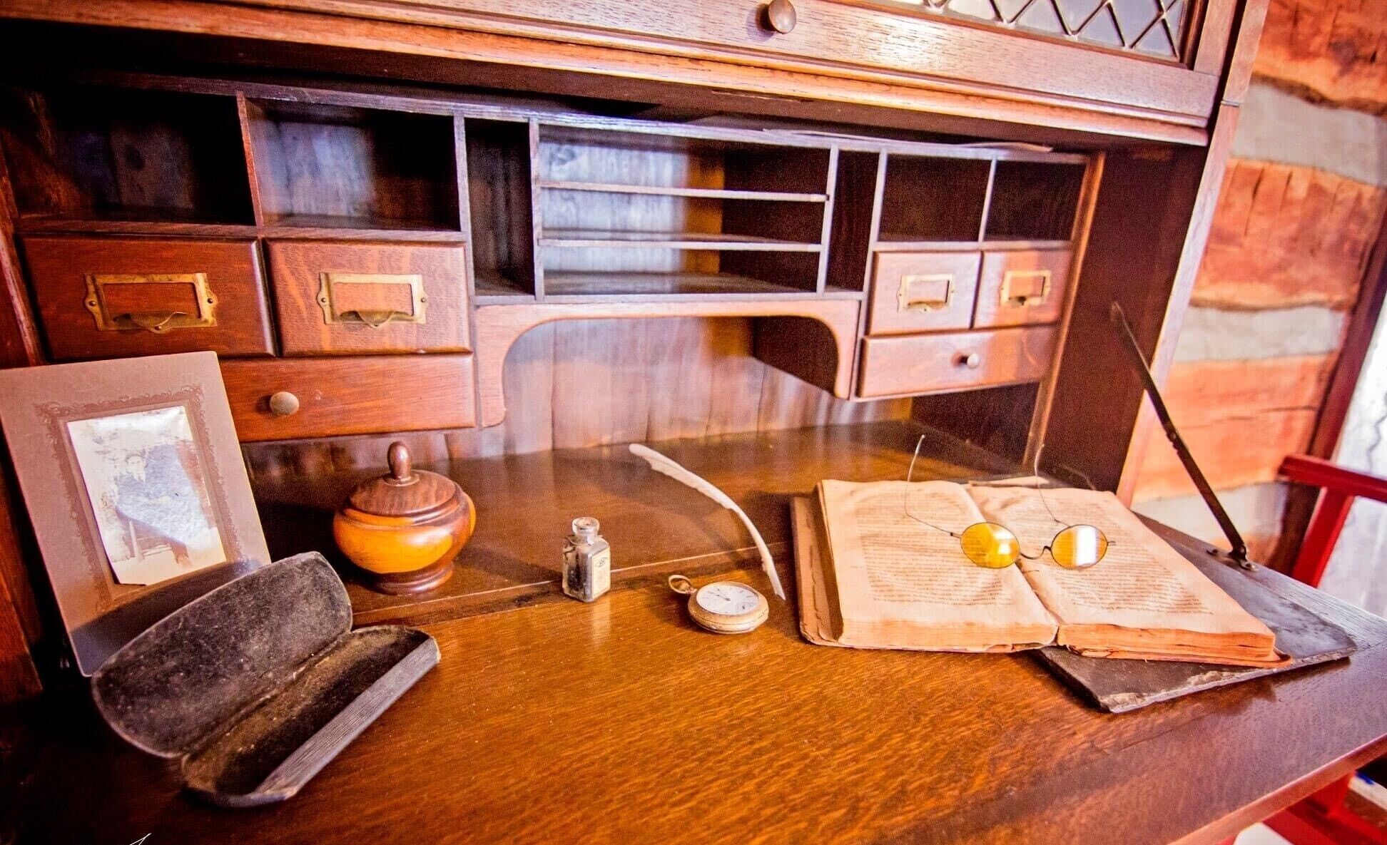 A wooden desk with drawers, a vintage compass, a book, and glasses.