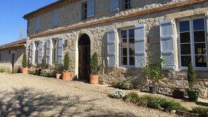 A stone building with a central arched entrance, multiple windows with shutters, and potted plants along the pathway. - La Maison de Campagne - Le Farat (Auvillar)