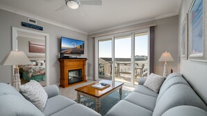A modern living room with a fireplace, comfortable seating, and a large window offering a view of the city. - Luxury 3 bedroom, 3 bath on the ocean with indoor and outdoor pools (Ocean City)