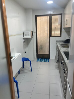 A compact kitchen with white tiled walls, a microwave, a sink, and a stove. - Tamaris playa 4ºC Solo Familias! (Playa Xeraco)