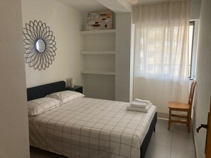 A bedroom with a bed, a chair, a nightstand, and a wall-mounted shelf. - Tamaris playa 4ºC Solo Familias! (Playa Xeraco)
