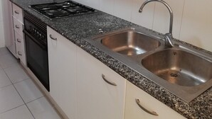 Cuina amb armaris blancs, fogó negre i rentapesos d'acer inoxidable.