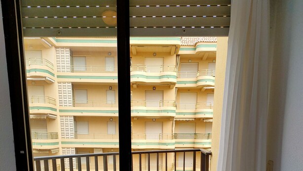 En balkon med seng og et sammenfoldet håndklæde, med udsigt til en bygning med flere balkoner.